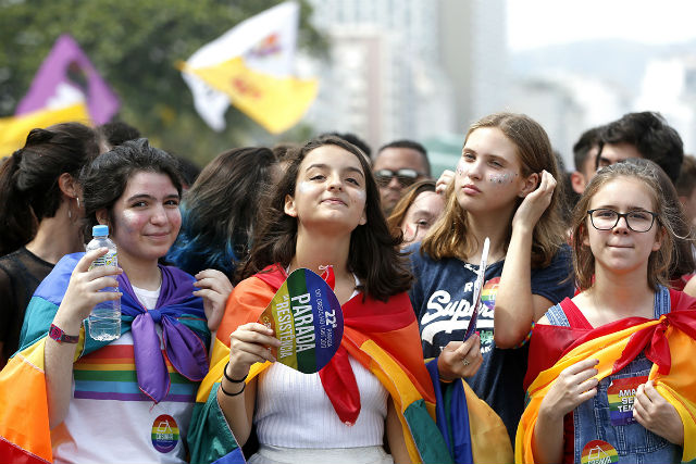 Grupo de meninas, vestindo bandeira LGBT, caminham durante a parada LGBT, pelo respeito à diversidade de gênero e de identidades