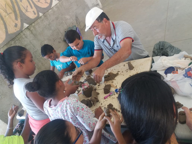 Crianças aprendem a esculpir em argila com um morador da comunidade
